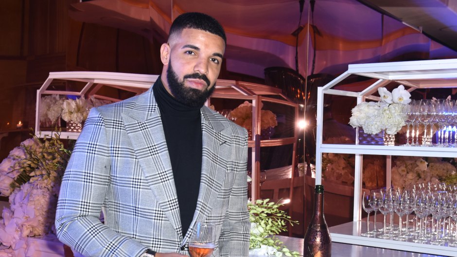 Drake wearing a gray suit drinking some chamapgne