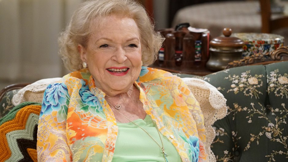 Betty White smiling while sitting on a couch wearing a floral blazer and green top