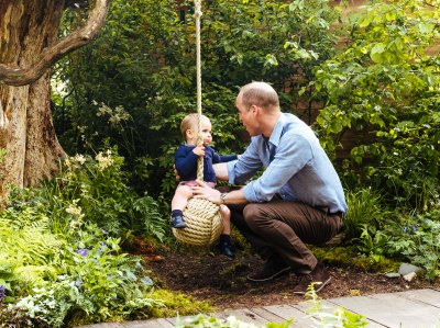prince william wears blue shirt and black pants while son louis sits on a swing wearing a navy blue sweater