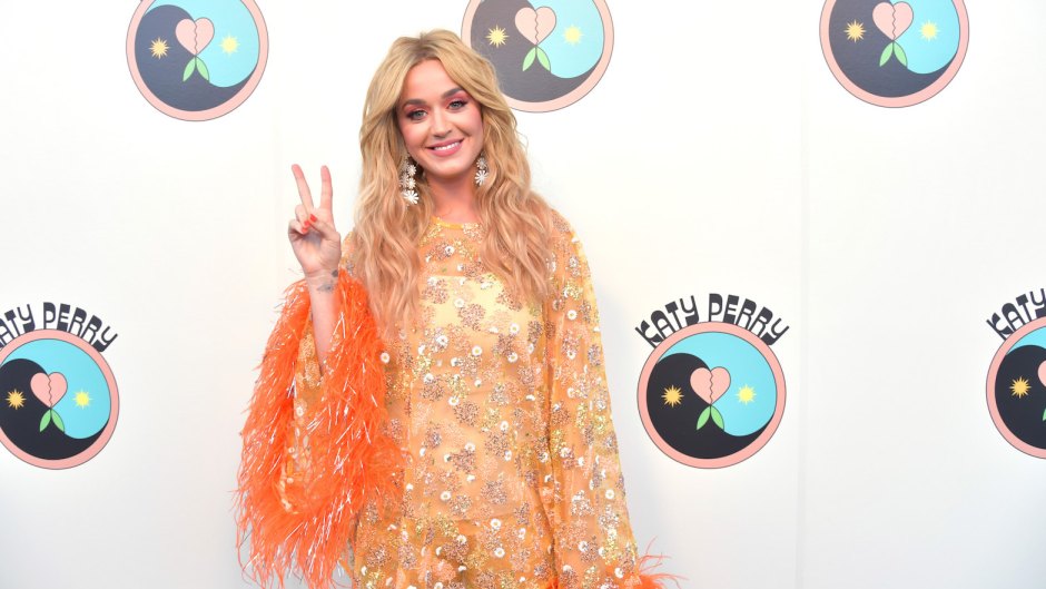 Katy Perry Wearing a Yellow and Orange Outfit and She Is Throwing Up a Peace Sign
