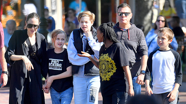 angelina jolie wears all black, daughter vivienne wears black t shirt and jeans, daughter shiloh wears a black puffy vest and a long sleeved gray sweatshirt with matching gray shorts, daughter zahara wears black t shirt and jeans and son knox wears black and white baseball tee with jeans while out at disney