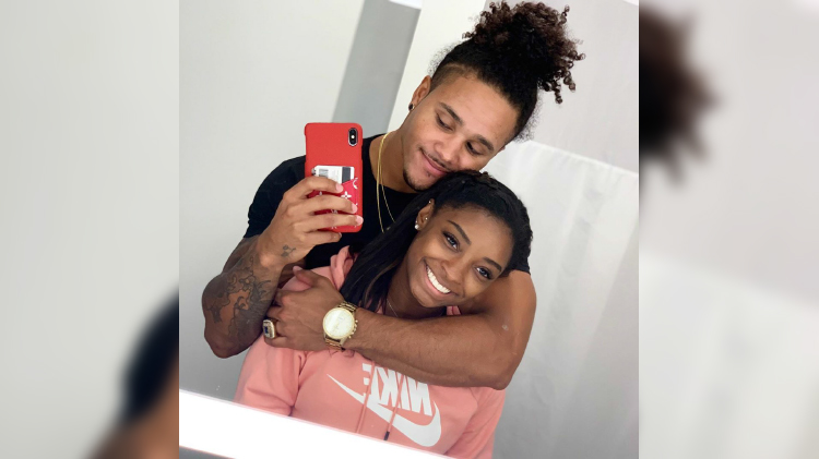 simone biles' boyfriend stacey ervin jr wears a black shirt and his long hair in a manbun while he wraps his arm around simone who is wearing a pink nike sweater with her hair straighted and pulled back in a half-up half-down look they both smile as stacey takes a mirror selfie in what seems to be a bathroom simone biles boyfriend seemingly supports her amid her brothers arrest