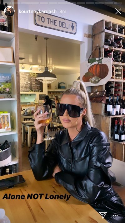 Khloe Kardashian Sitting at Table Drinking Alcohol Indoor Restaurant With Wine Collection and Deli