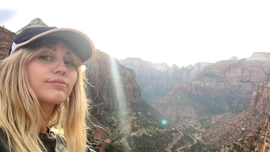 miley cyrus wears a hat and black t shirt in a selfie with mountains in the background miley cyrus seemingly shades exes in message about love on instagram