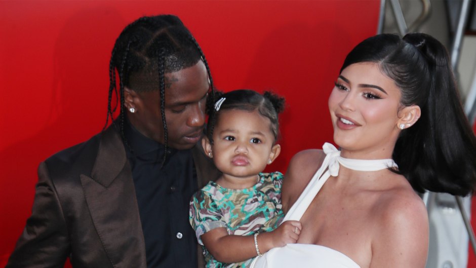 kylie jenner wears a white dress and travis scott wears a black button down shirt underneath a brown suit and stormi webster wears a matching bright green camouflage matching shirt and pants set kylie jenner and travis scott are coparenting stormi