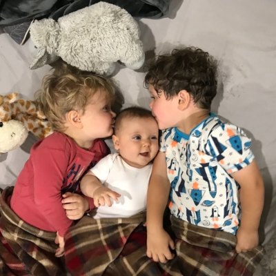 spurgeon and henry seewald lying on a bed kissing the sides of their little sister's head