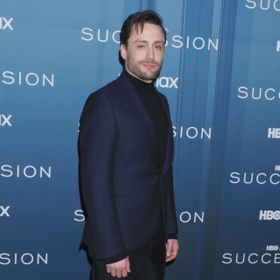 Kieran Culkin poses in front of a blue Succession backdrop while wearing a navy suit.