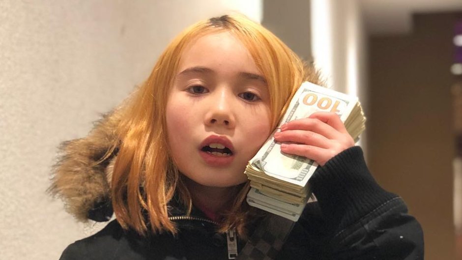 Lil Tay holding a wad of cash and wearing a black winter coat