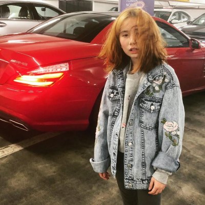 A picture of Lil Tay standing in front of a red car