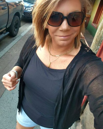Meri Brown taking a selfie wearing a black cardigan and blue shorts
