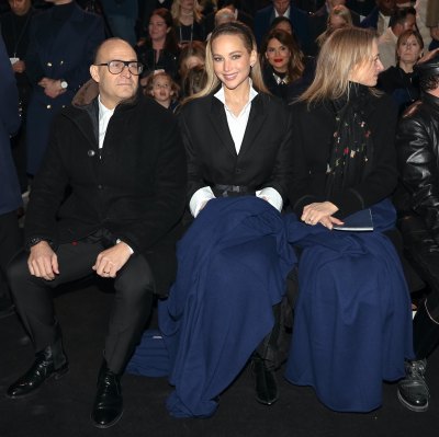 Jennifer Lawrence wearing a black coat over a white button down shirt sitting between Marc Metrick and Delphine Arnault at the Saks Fifth Avenue lighting ceremony.