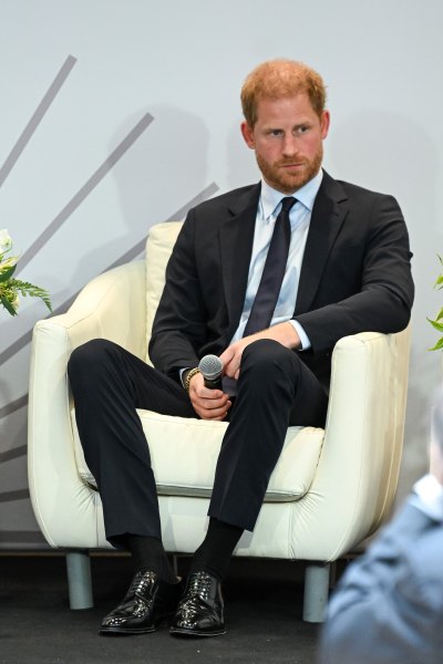 Prince Harry wears a black suit while sitting in a white chair