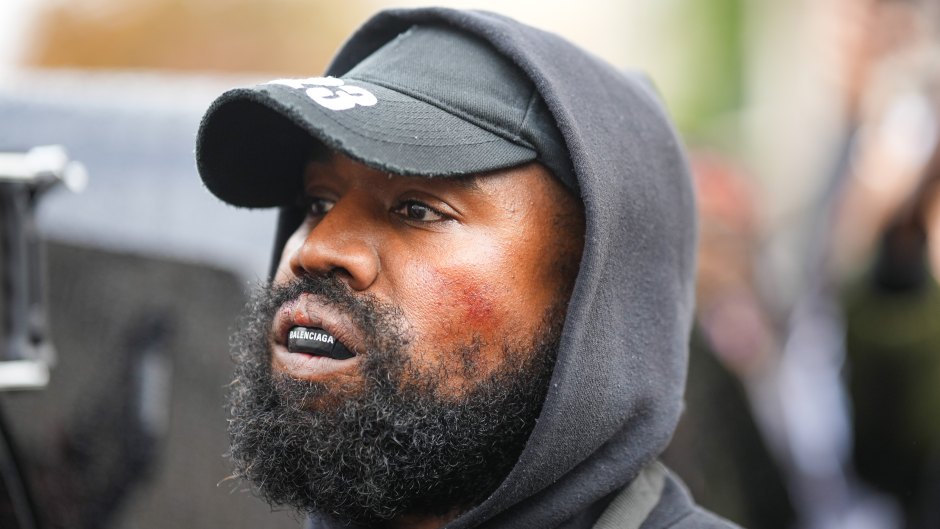 Kanye West wearing a black hoodie and black baseball cap while wearing a Balenciaga mouthguard over his teeth.