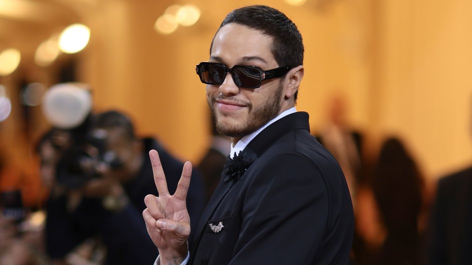 Pete Davidson gives a peace sign while wearing sunglasses and a suit