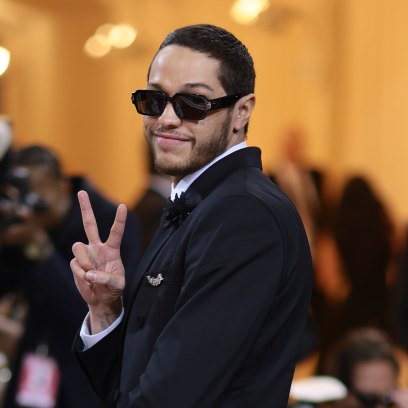 Pete Davidson gives a peace sign while wearing sunglasses and a suit