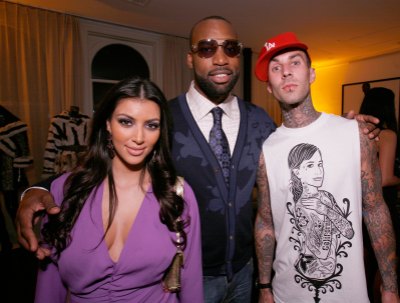 Kim Kardashian in a purple dress poses next to Baron Davis and Travis Barker