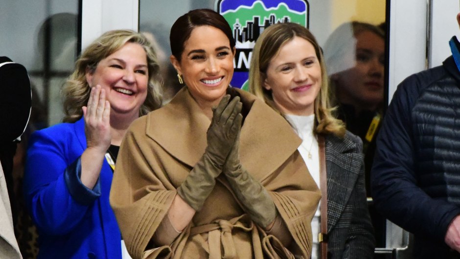 Meghan Markle smiles while wearing a tan coat and brown leather gloves